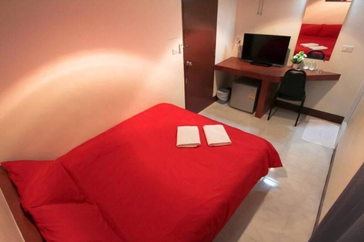 Kompakti hotellihuone, jossa on punainen sänky, työpöytä, jossa on televisio, ja pieni oleskelualue.