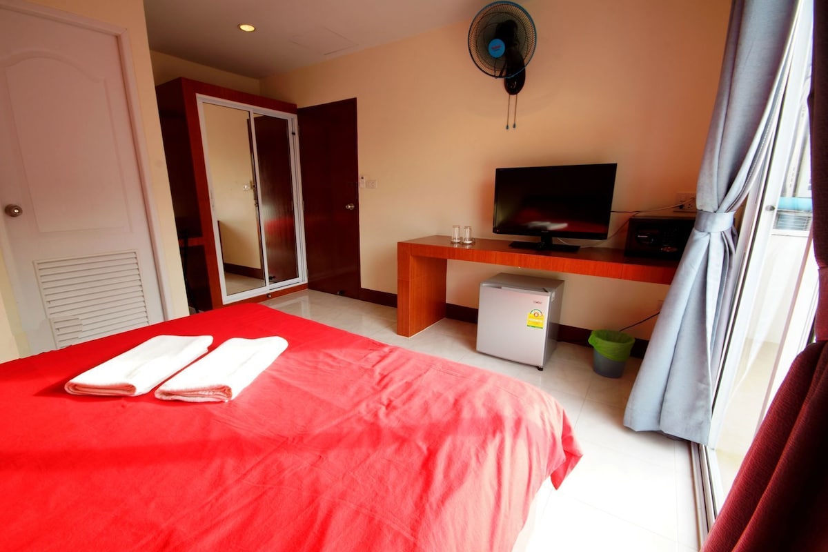 A hotel room with a bed, a desk with a television, a mini-fridge, and a sliding door closet.