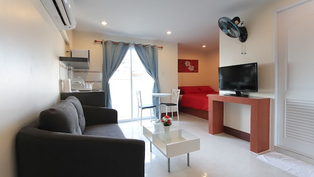 A modern living room with a sofa, a coffee table, a TV on a stand, and a dining area with chairs and a table. - Walking Street Guest House (Pattaya)