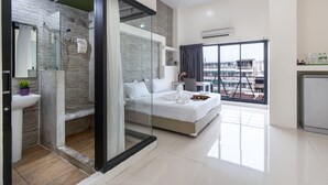 A modern hotel room with a glass shower enclosure, a large bed, a bedside table, and a view of the city through a large window. - Baron Zotel Bangkok (Bangkok)