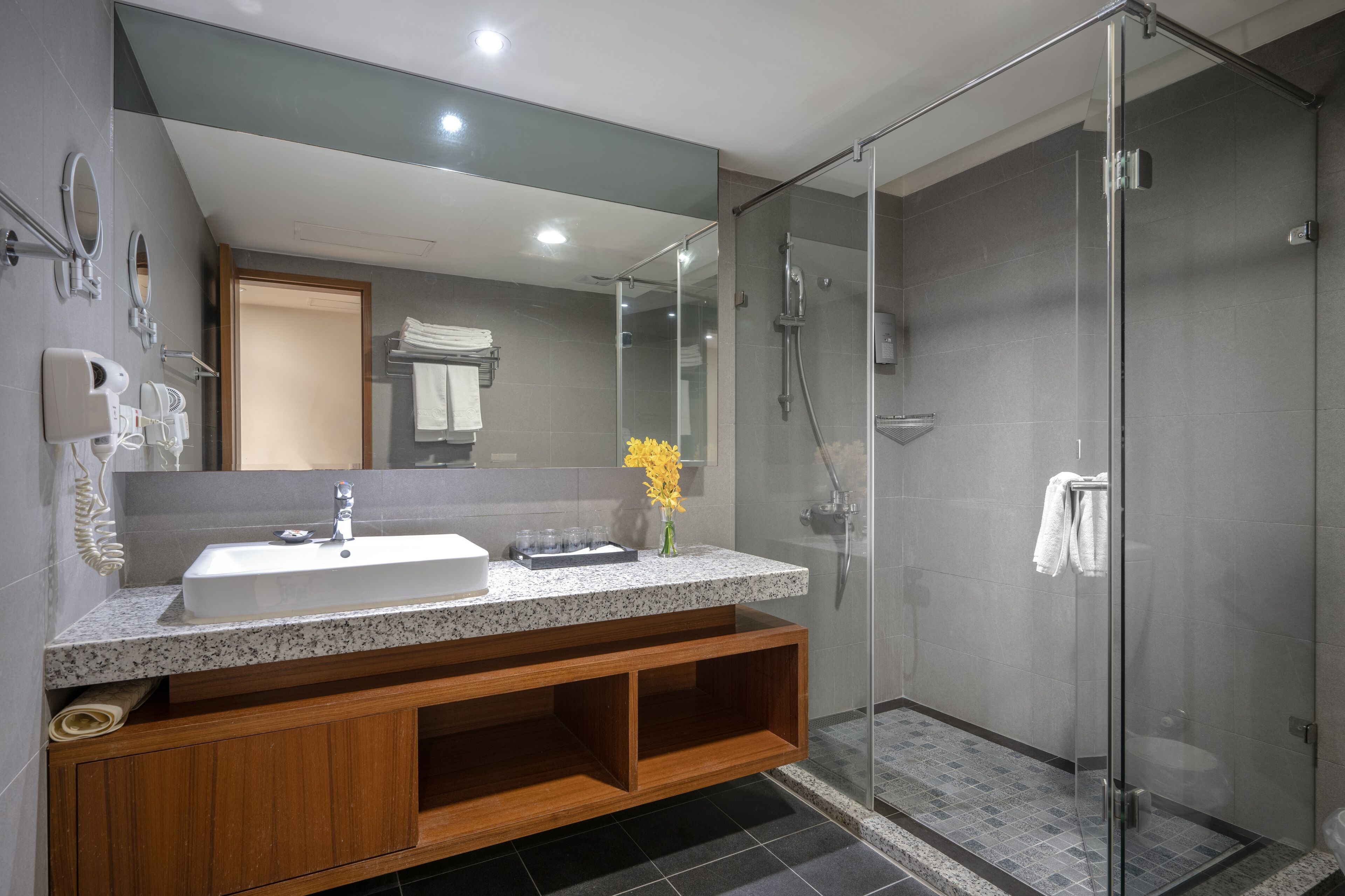 A modern bathroom with a granite countertop sink, a glass shower enclosure, and a wooden vanity.