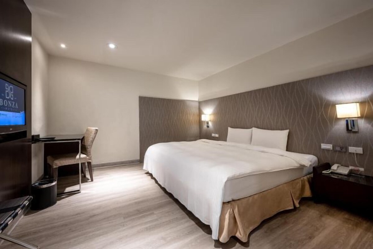 Habitación de hotel con una cama grande, un escritorio con silla, televisión y una lámpara de pared.