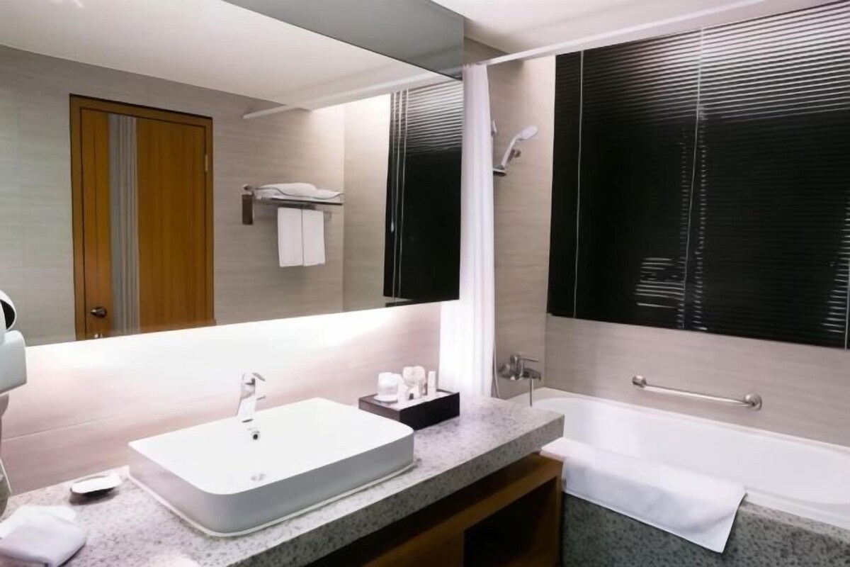A modern bathroom with a large mirror, a white sink, a bathtub, and a shower area.