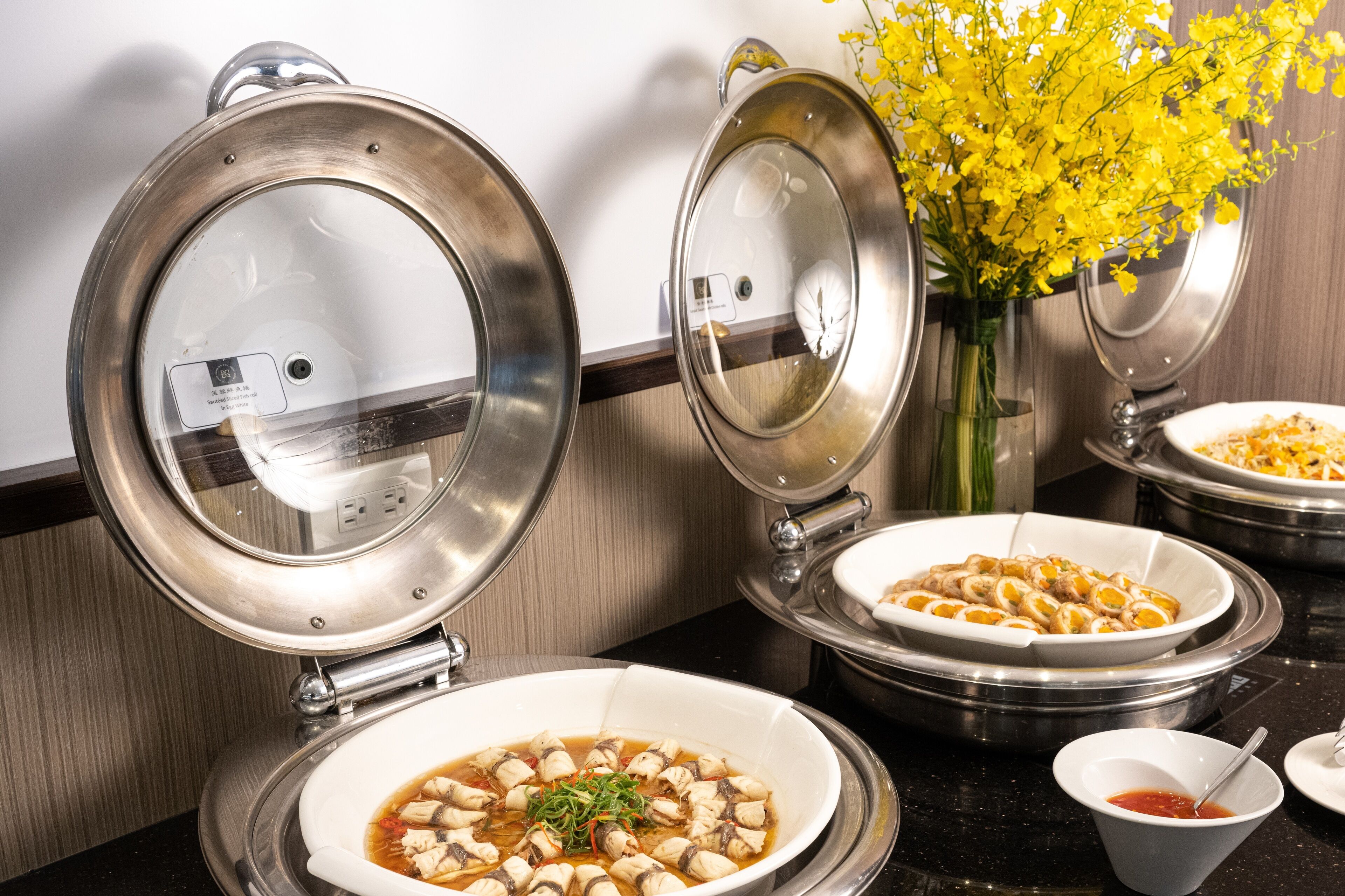 A buffet setup with various dishes, including a bowl of soup and a dish with sliced meat, in a modern kitchen setting.