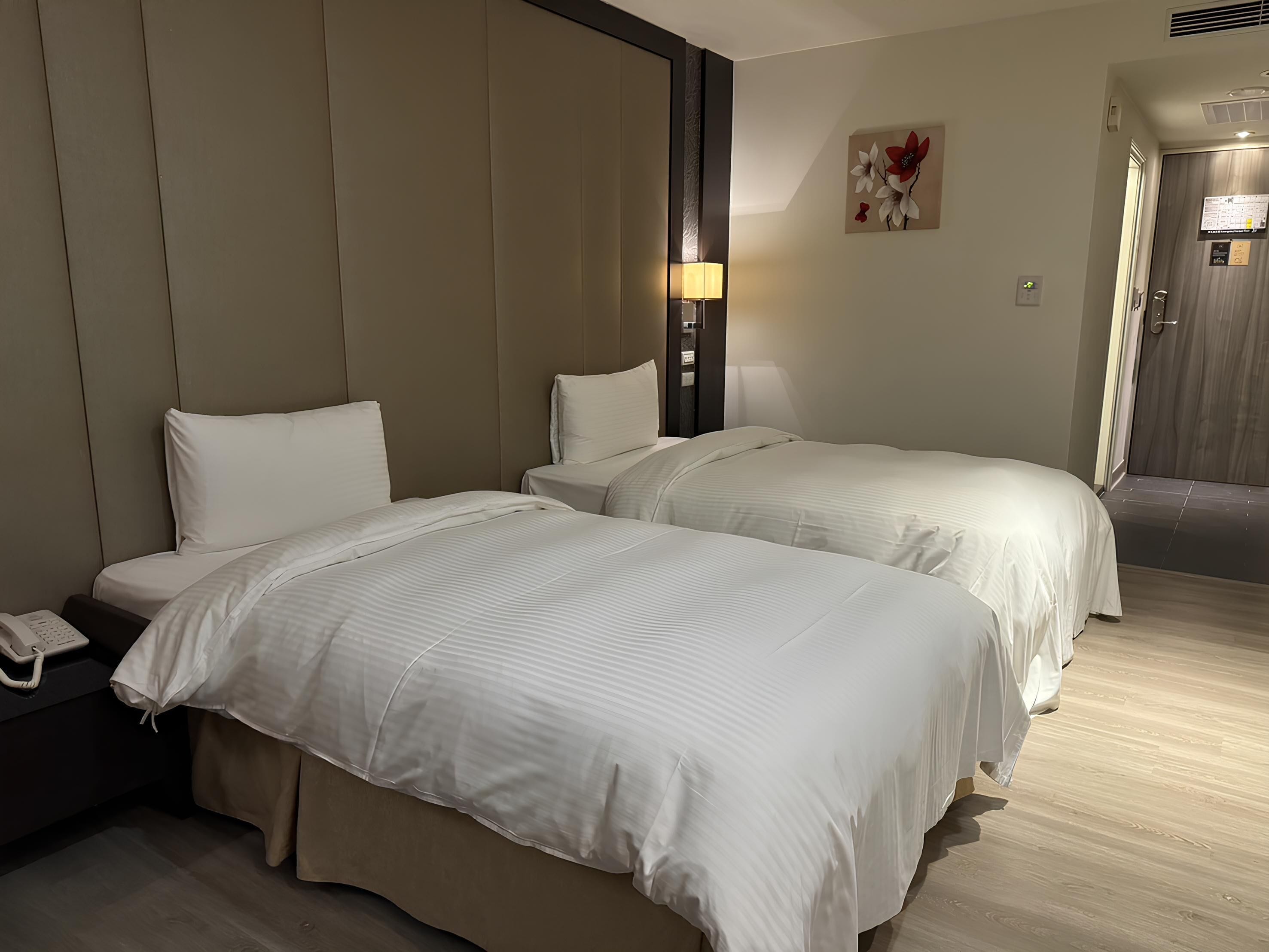 A hotel room with two beds, a bedside phone, a lamp, and a wall-mounted artwork.