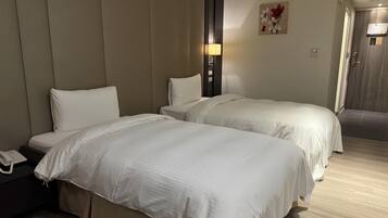 A hotel room with two beds, a bedside phone, a lamp, and a wall-mounted artwork.