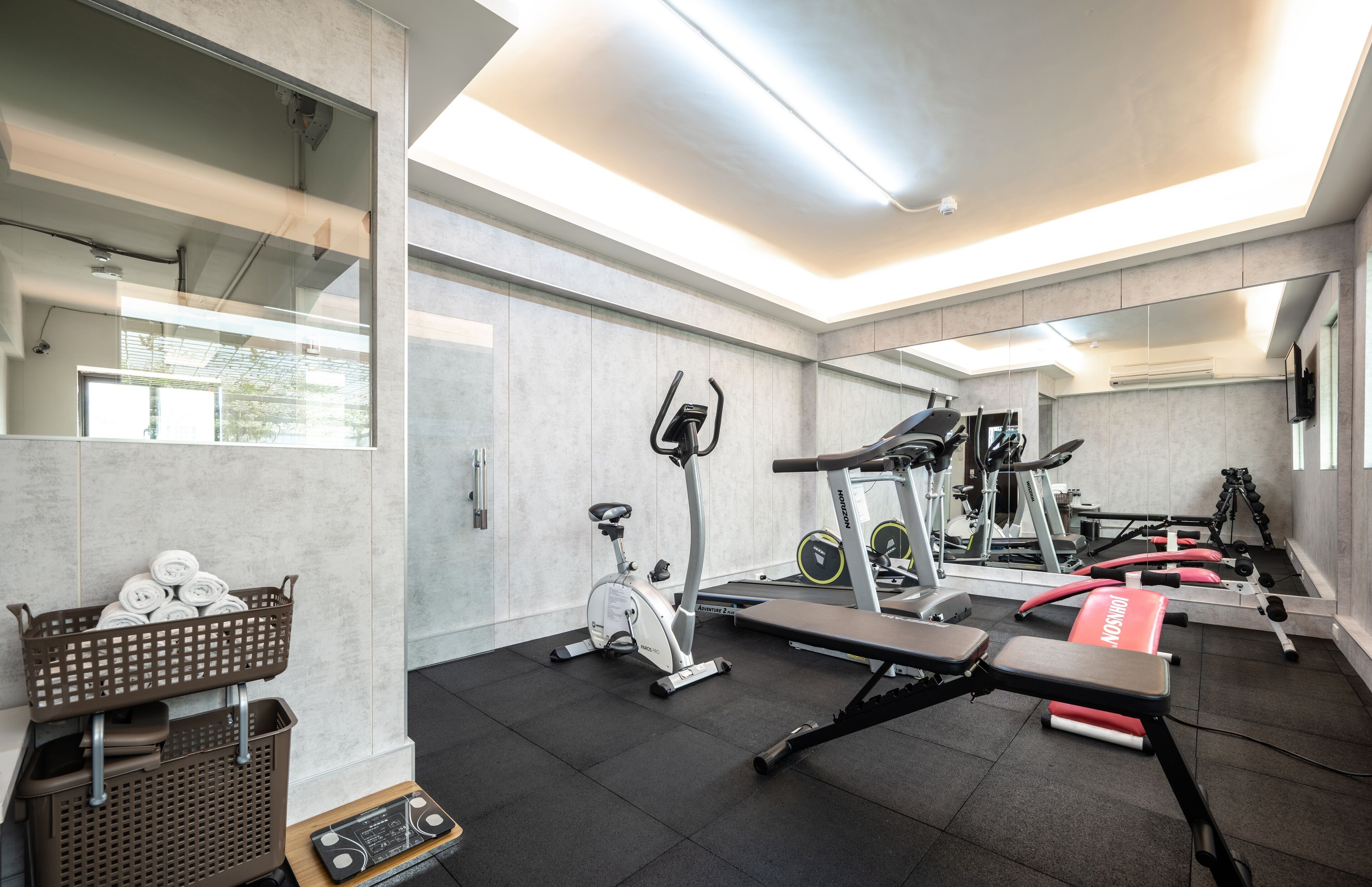 Une salle de sport moderne équipée de matériel d’exercice, d’un banc et d’un panier rempli de serviettes.