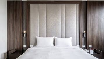 Habitación de hotel con una cama grande, paneles de madera en las paredes y cabecera en tonos neutros. Se observan mesitas de noche con lámparas y un teléfono a un lado.