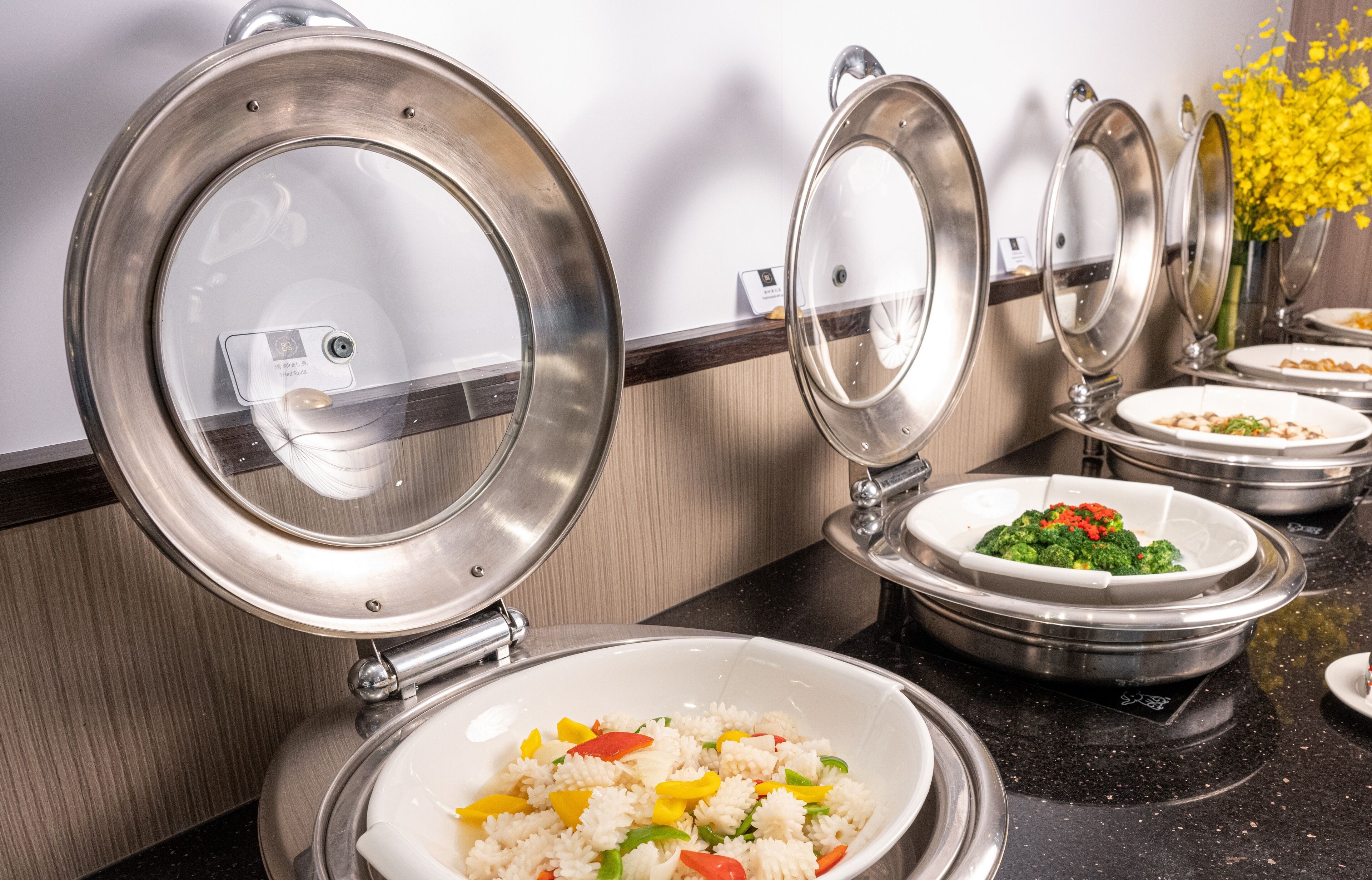 A buffet setup with multiple bowls of food, including pasta and vegetables, and a stainless steel sink.