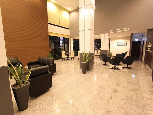 A modern lobby with black leather sofas, a reception desk, and potted plants.