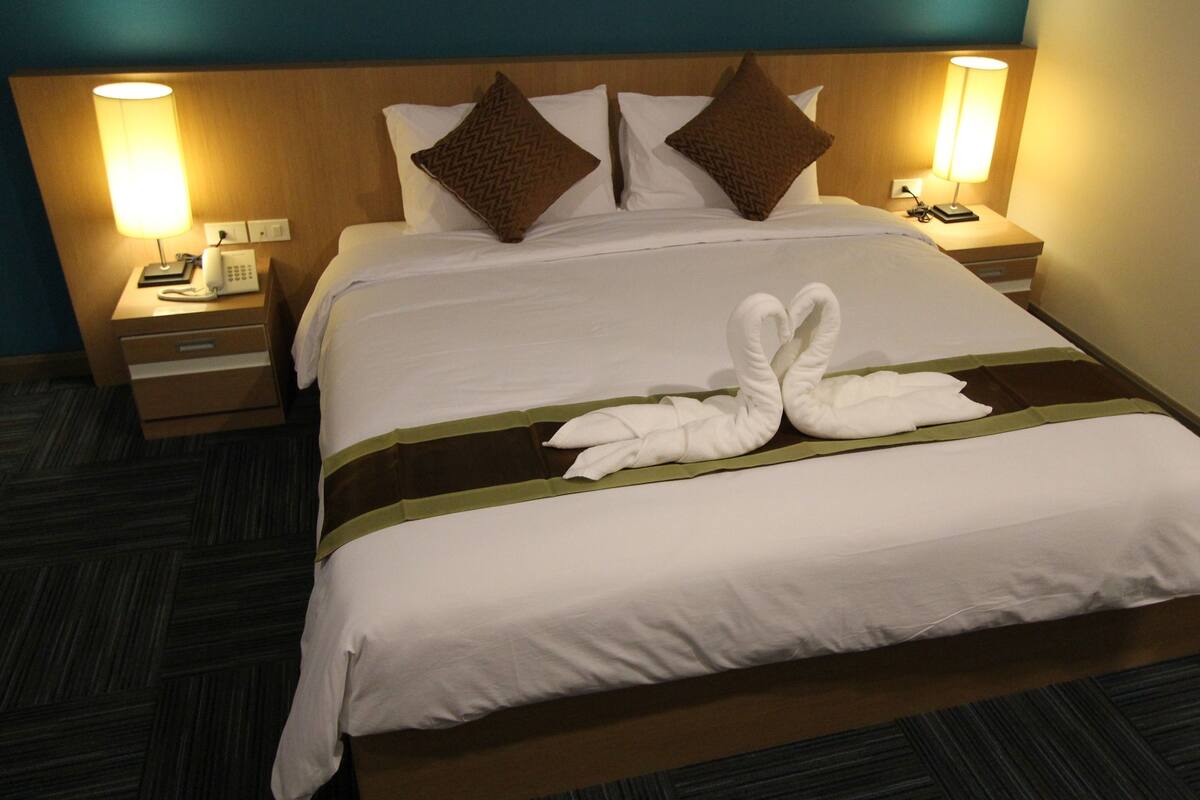 A hotel room with a neatly made bed, two pillows, a bedside table with a lamp, and a telephone.