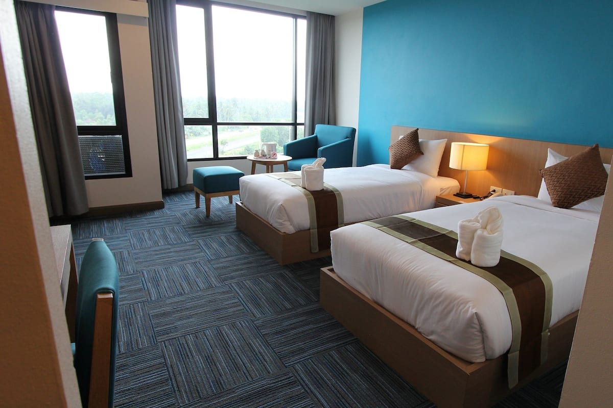 A hotel room with two beds, a small table, a chair, and a view of the outdoors.