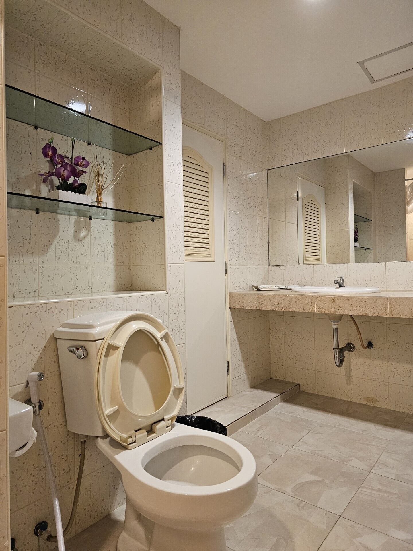 Een badkamer met toilet, wastafel, spiegel en een glazen plankje met decoratieve spullen.