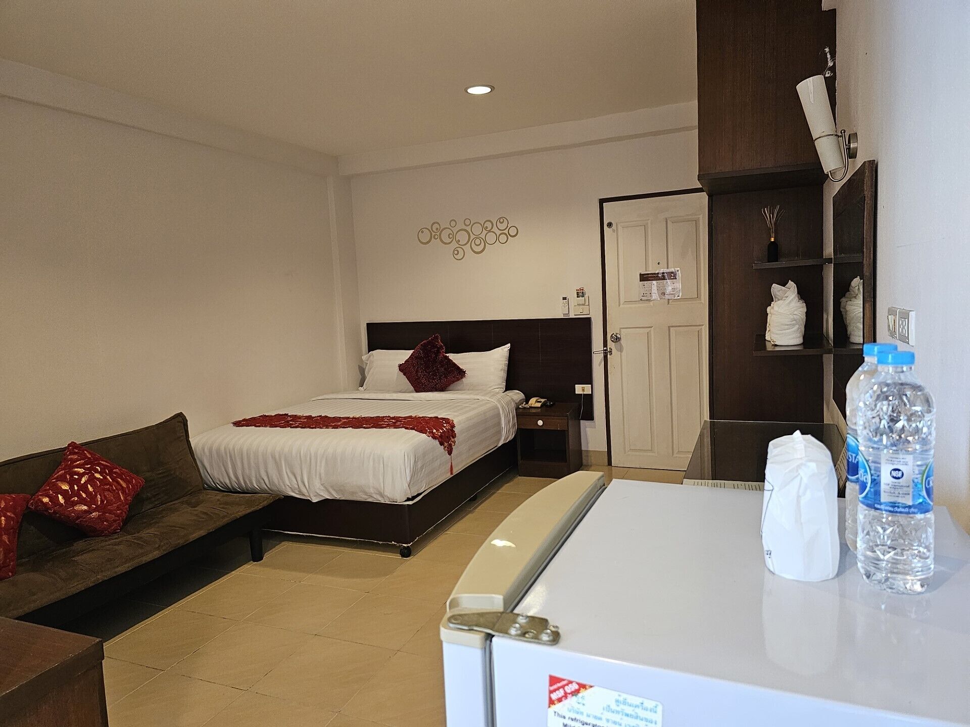A hotel room with a bed, a sofa, a desk with a refrigerator, and a water dispenser.