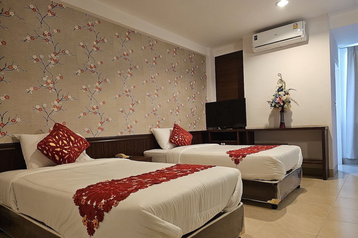 A hotel room with two beds, a TV, an air conditioner, and a floral wall decoration.