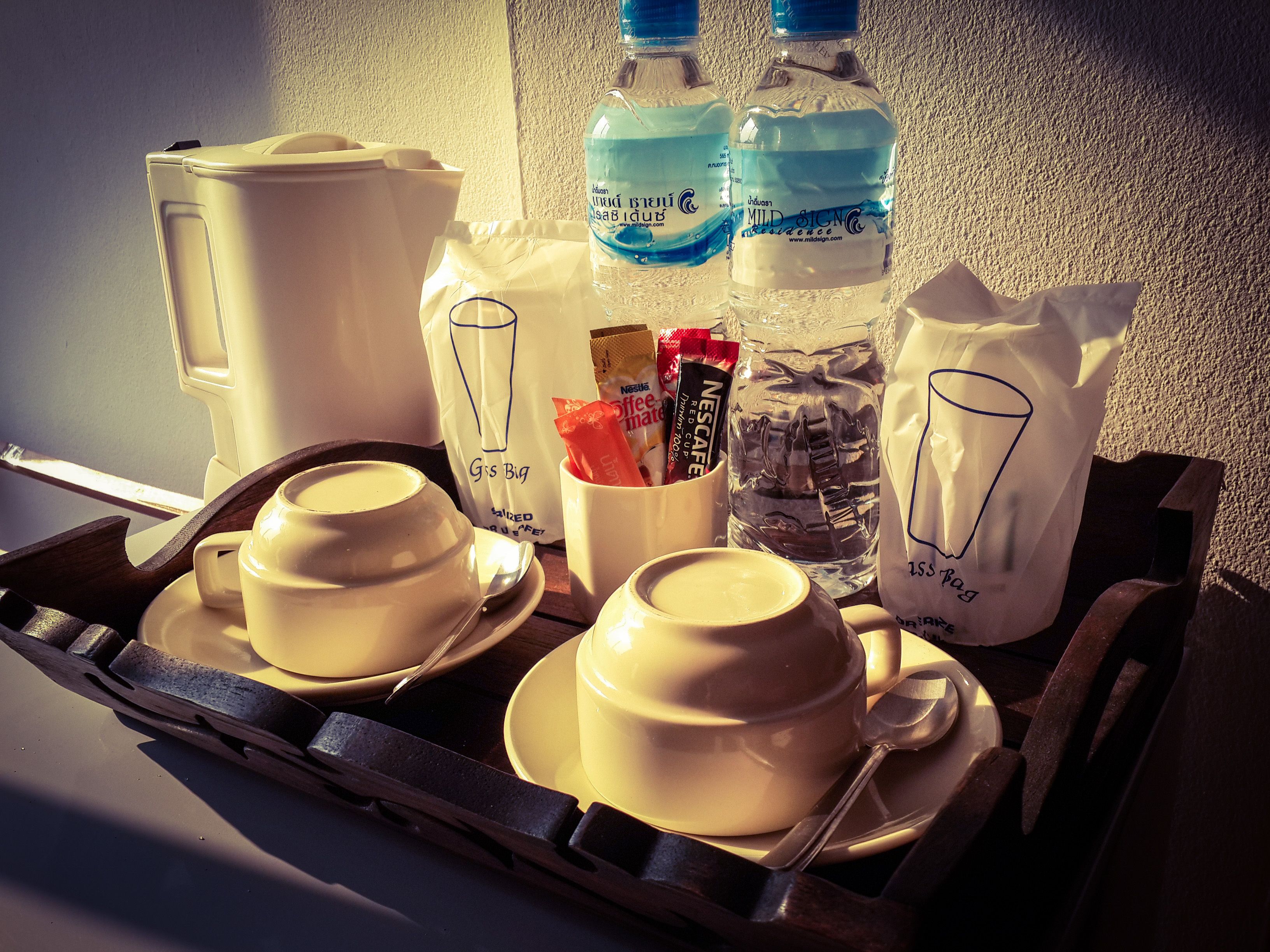 A tray with two cups of coffee, a glass of water, a coffee maker, and a bag of coffee creamer.