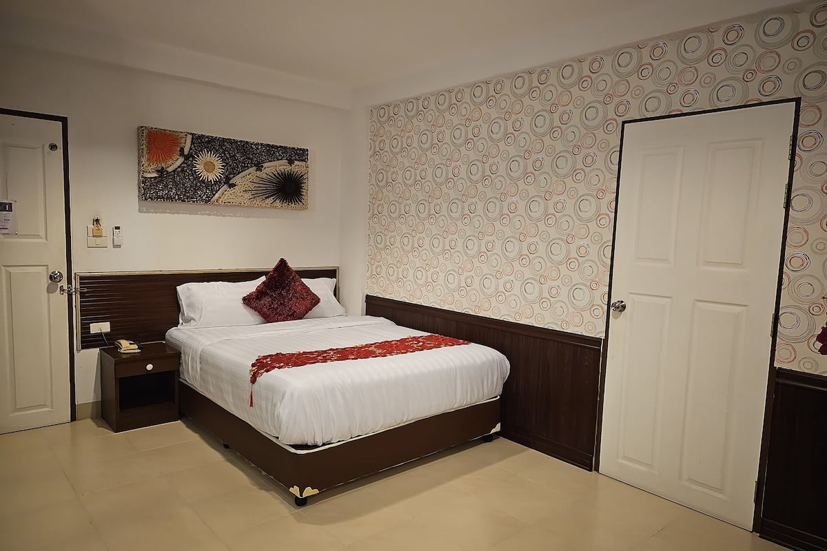 A hotel room with a bed, a nightstand, a wall-mounted artwork, a patterned wallpaper, and a door.