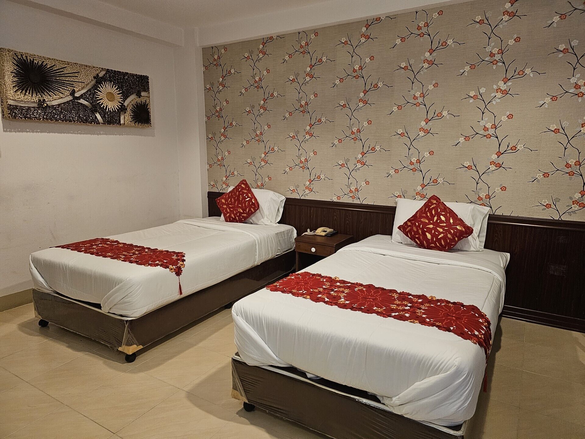 A hotel room with two beds, a wooden headboard, a floral wallpaper, and a decorative wall piece.