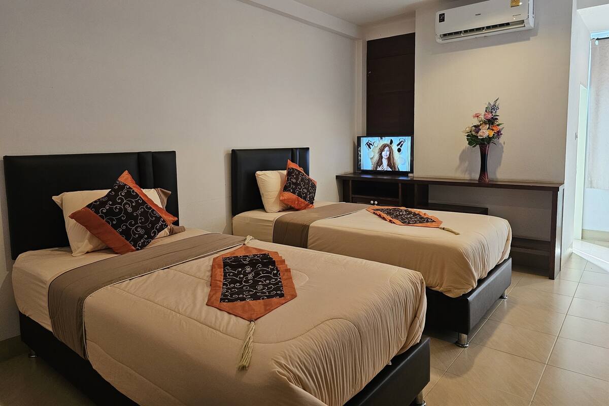 A hotel room with two beds, a TV, an air conditioner, and a vase with flowers.