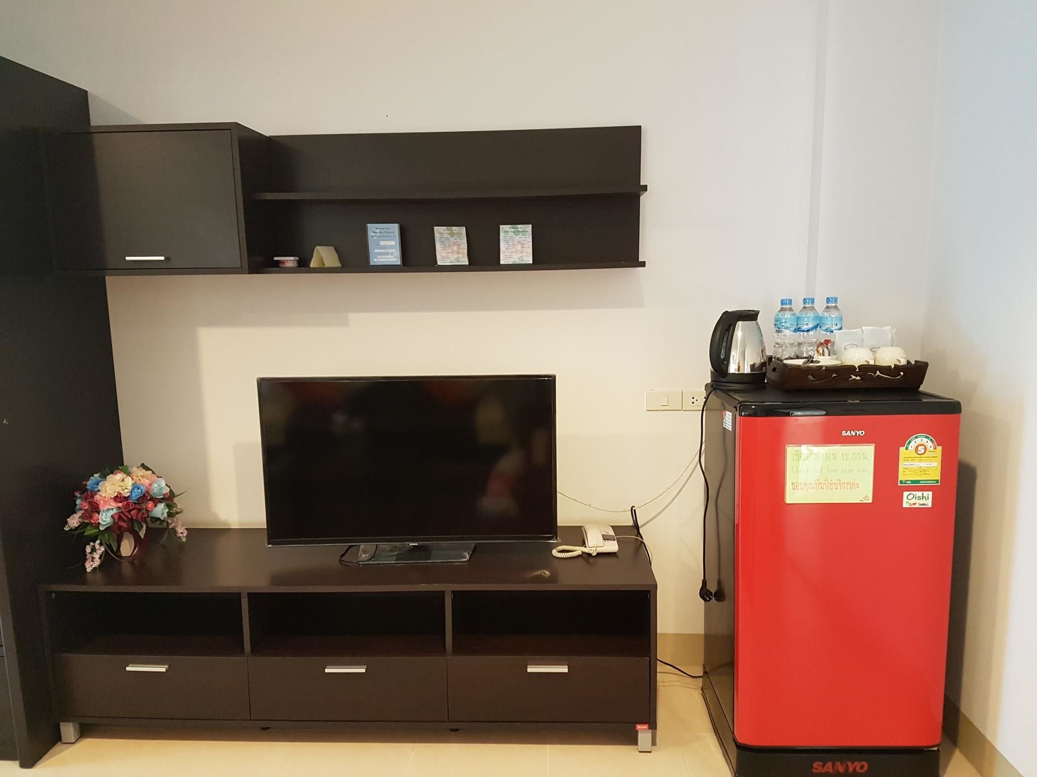 A modern living room with a flat-screen TV on a black entertainment unit, a red refrigerator, and a small shelf with items.