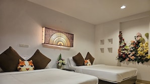 Una habitación de hotel con dos camas, cada una con almohadas marrones y con motivos de gatos. Hay una obra de arte colgada en la pared sobre las camas y un arreglo floral también en la pared.