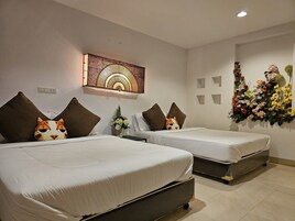 A hotel room with two beds, each with brown pillows and a cat-themed pillow. There is a wall-mounted artwork above the beds and a floral arrangement on the wall.