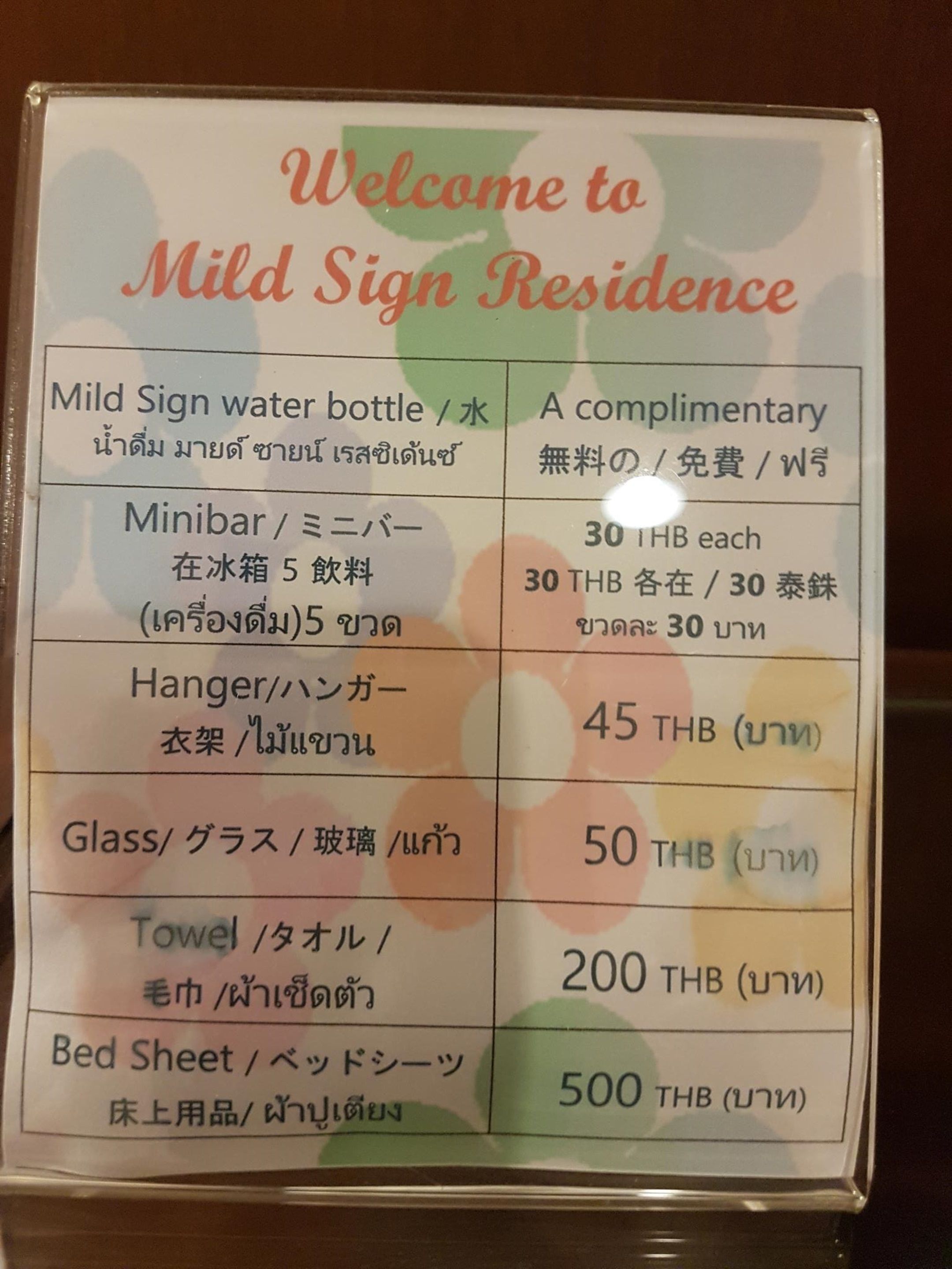 Een welkomstbord voor Mild Sign Residence met een overzicht van voorzieningen en hun prijzen in Thaise baht.