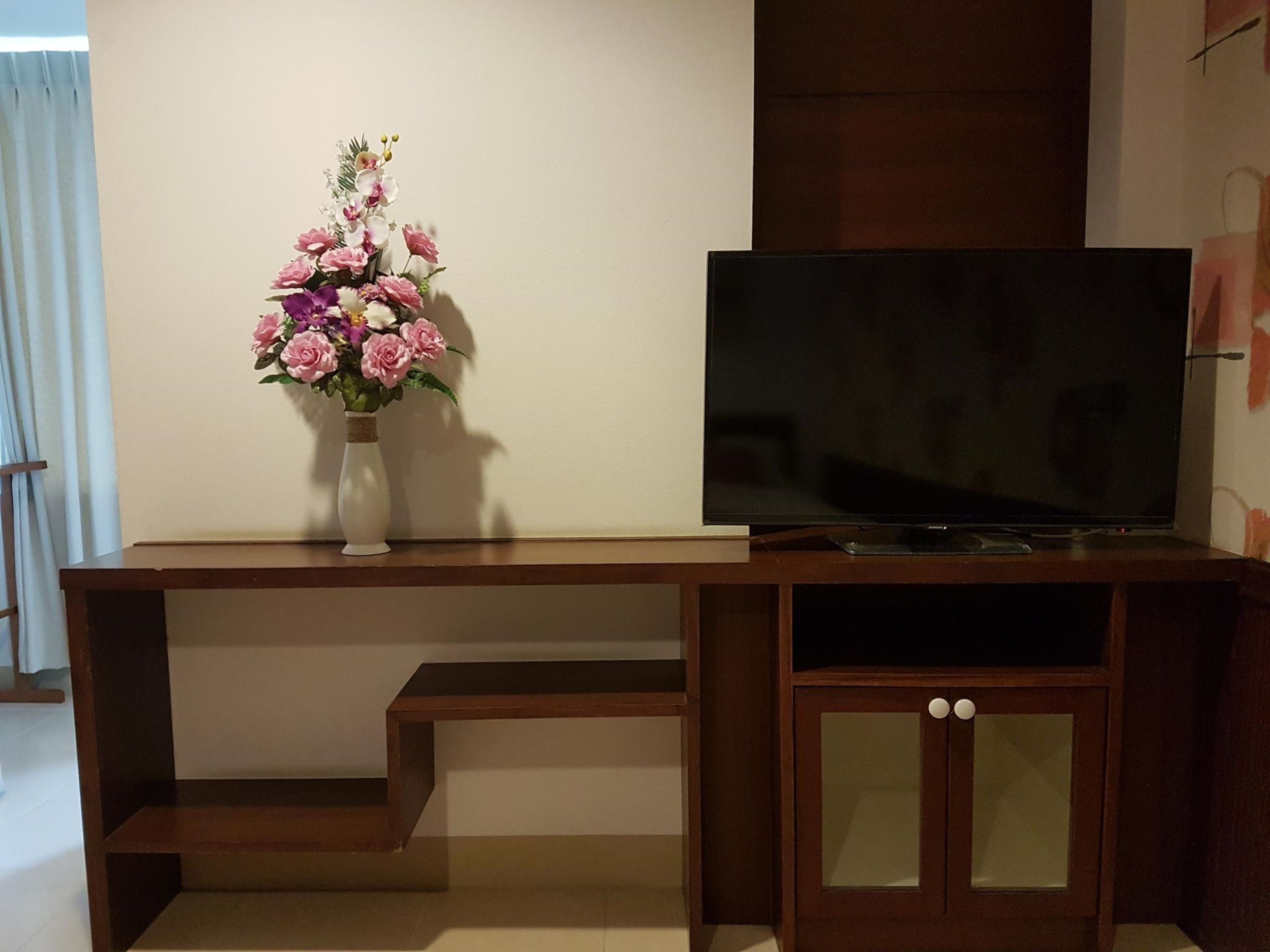 A wooden entertainment unit with a flat-screen TV and a vase of flowers.