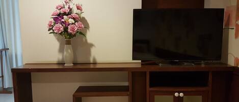 A wooden entertainment unit with a flat-screen TV and a vase of flowers.