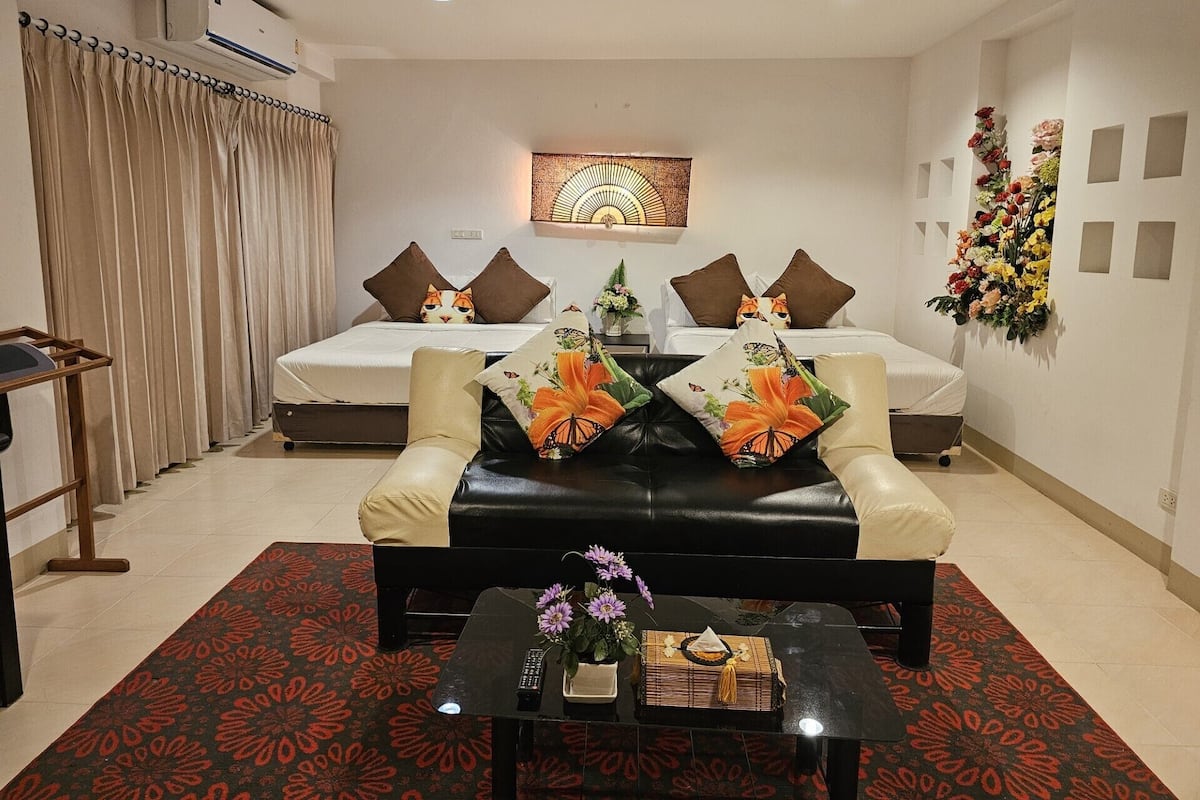 A hotel room with two beds, a sofa, a coffee table, and a decorative wall piece.