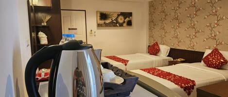 A hotel room with two beds, a kettle, a small table, and a decorative wall.