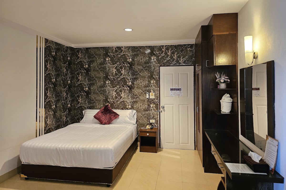 A hotel room with a bed, a nightstand, a desk with a mirror, a door, and a wall with a marble-like pattern.