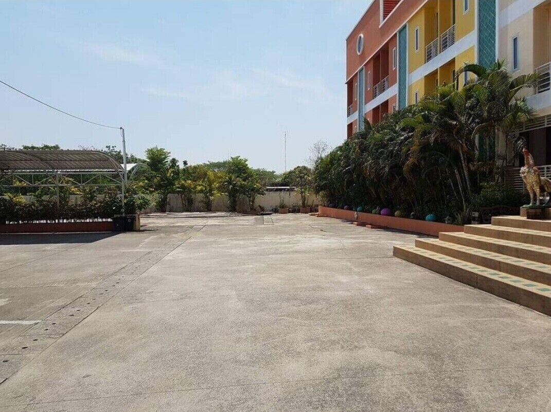 A spacious outdoor area with a concrete floor, surrounded by a low wall and a building with balconies.