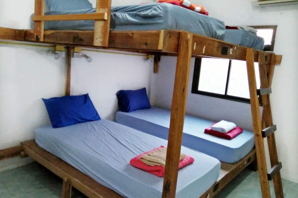 A bunk bed room with a wooden frame, two lower beds, and a top bunk.