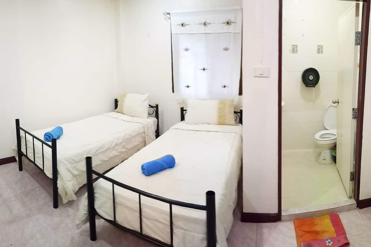 A small, clean room with two single beds, a bathroom with a toilet and sink, and a glass shower door.