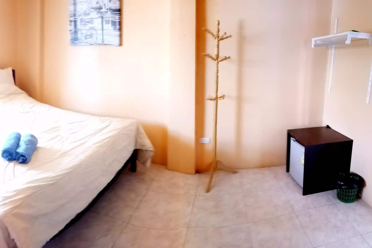 A hotel room with two beds, a small table, a trash bin, and a coat rack.