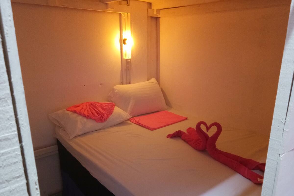 A small, single-bed room with white walls and a simple bed setup.