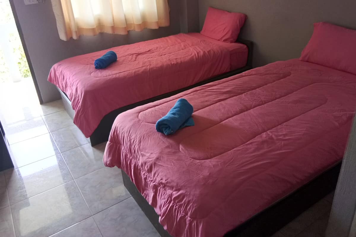 Two single beds with pink bedding and blue towels, a grey wall, and a window with curtains.
