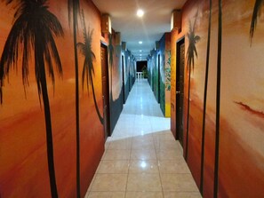 A hallway with palm tree murals on the walls, leading to a bright room. - Wild & Wandering Backpacker & Bar (Ko Pha-ngan)