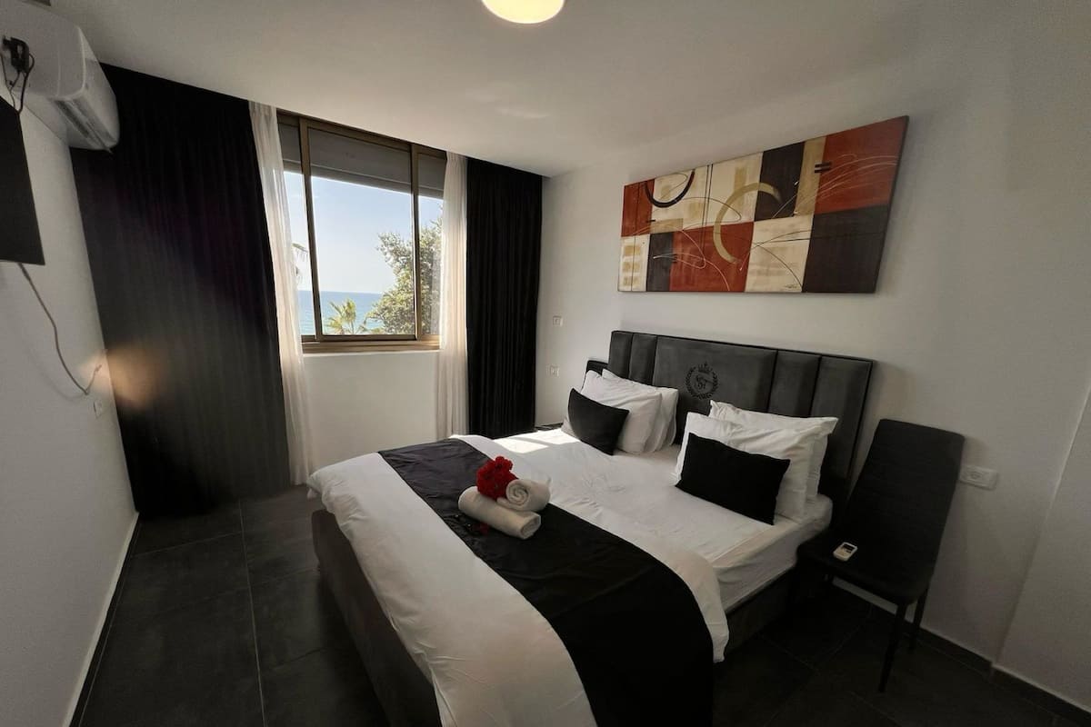 A modern hotel room with a large bed, a view of the outdoors, and a painting on the wall.