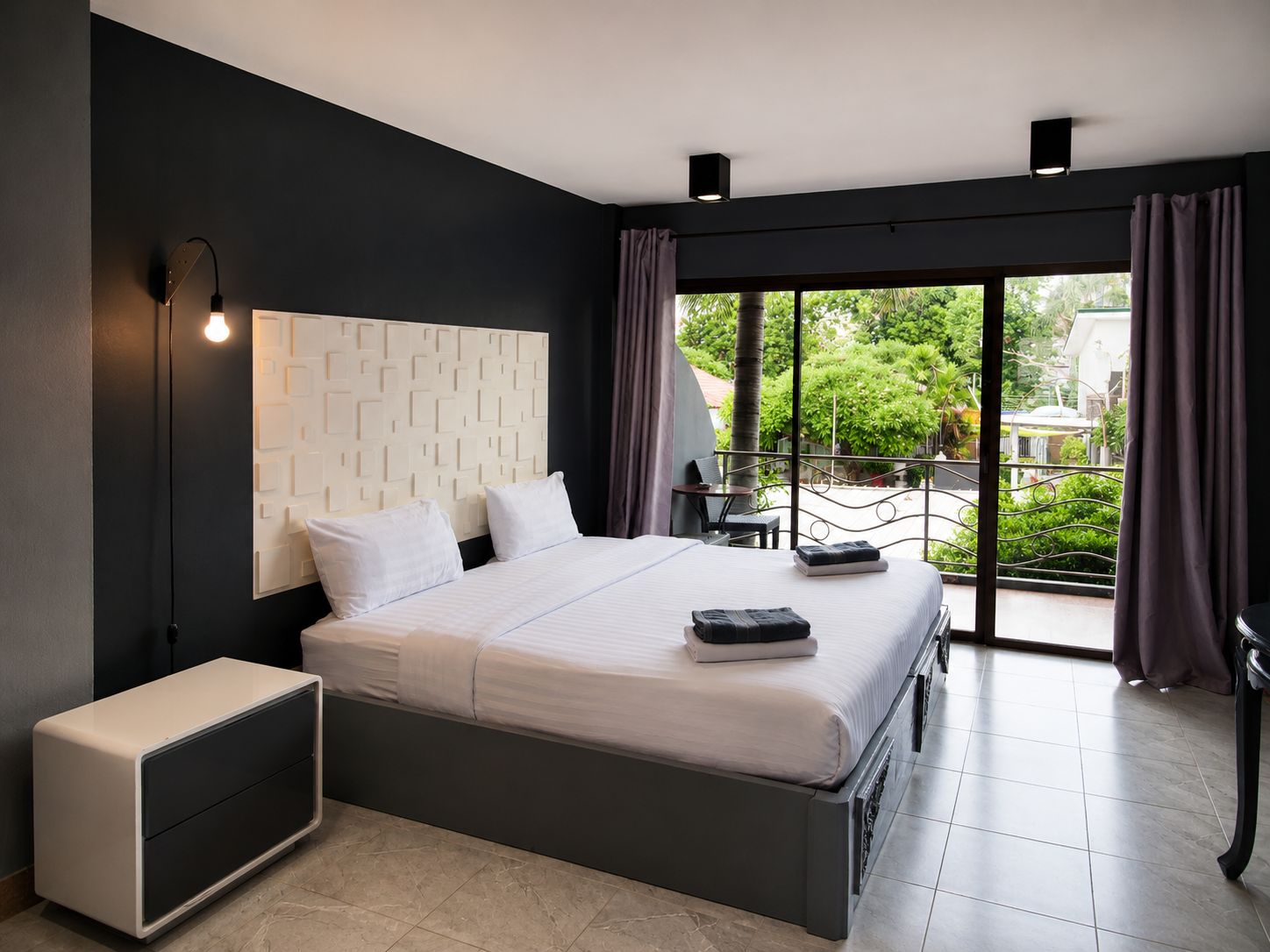 Une chambre à coucher moderne, dotée d’un grand lit, d’une table de chevet, d’une commode et offrant une vue sur l’extérieur grâce à un balcon.