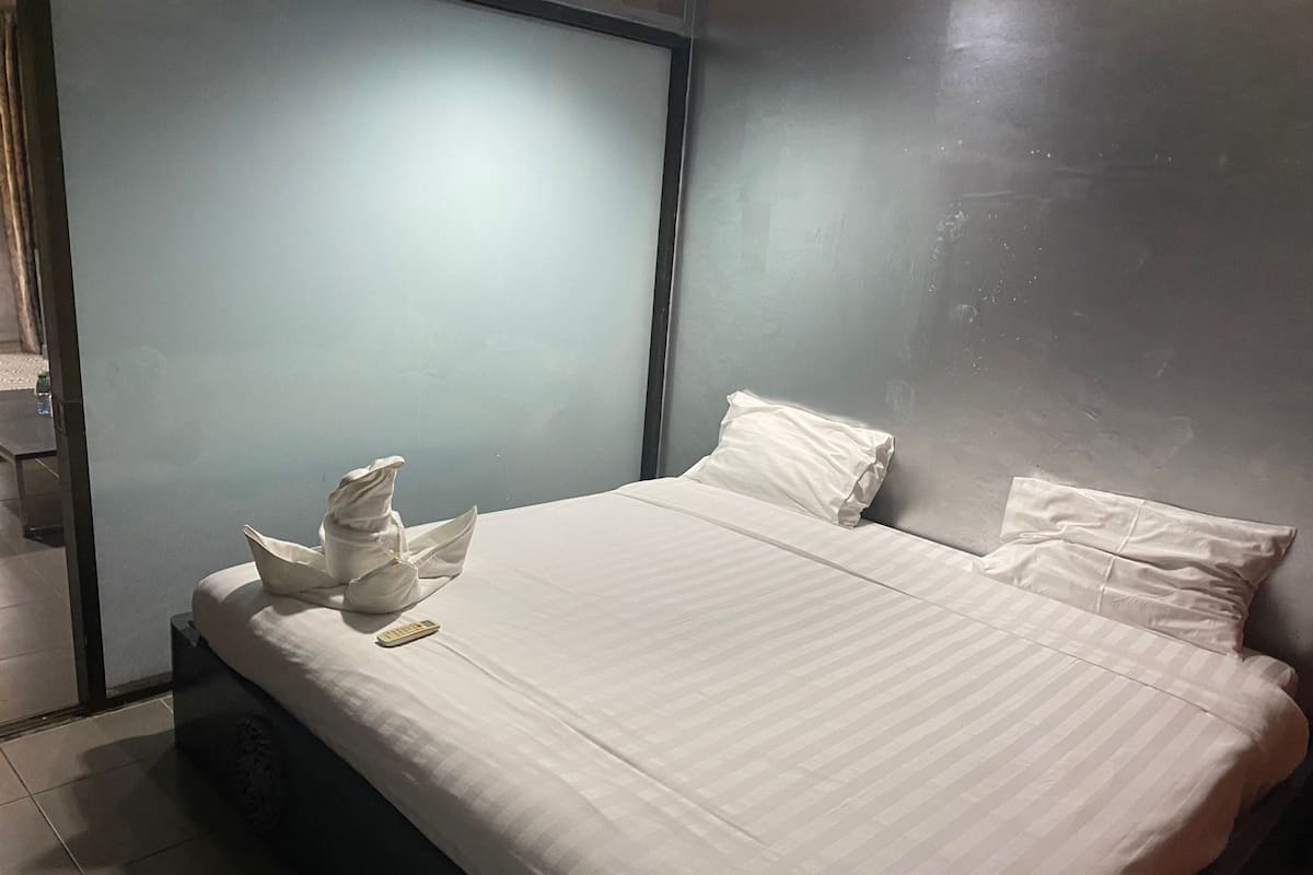 A neatly made bed with white linens and pillows, a remote control, and a folded towel on the left side.