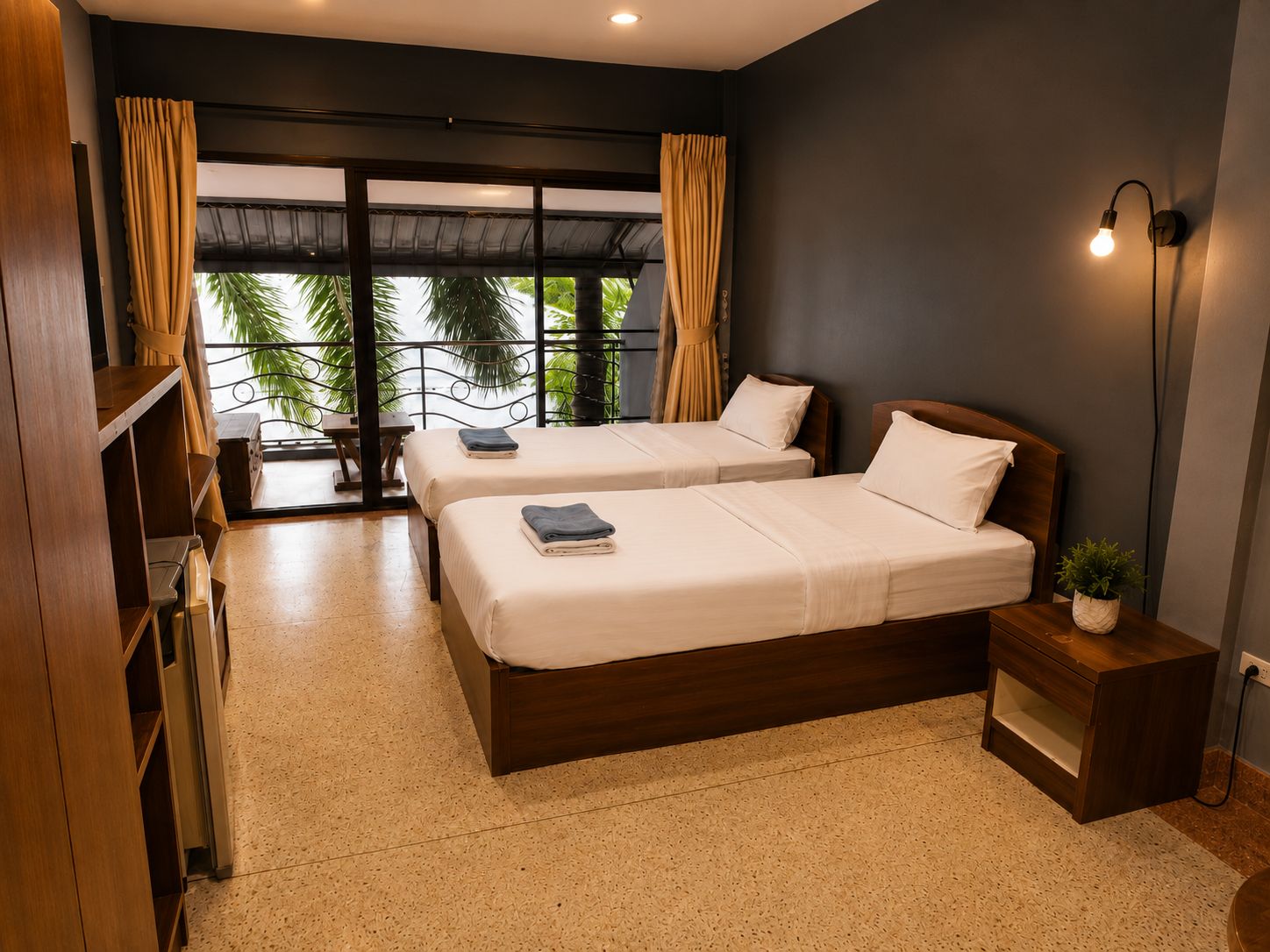 A hotel room with two beds, a small bedside table, a nightstand, a lamp, and a view of palm trees through large windows.