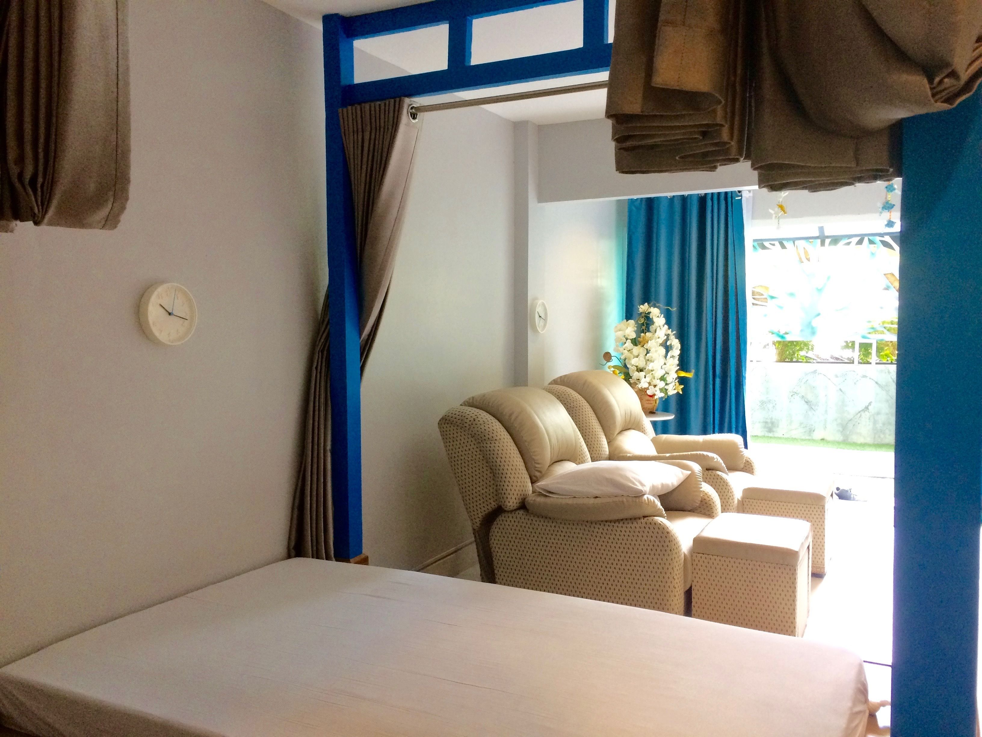 A hotel room with a bed, a chair, a small table, a clock, and a window with curtains.