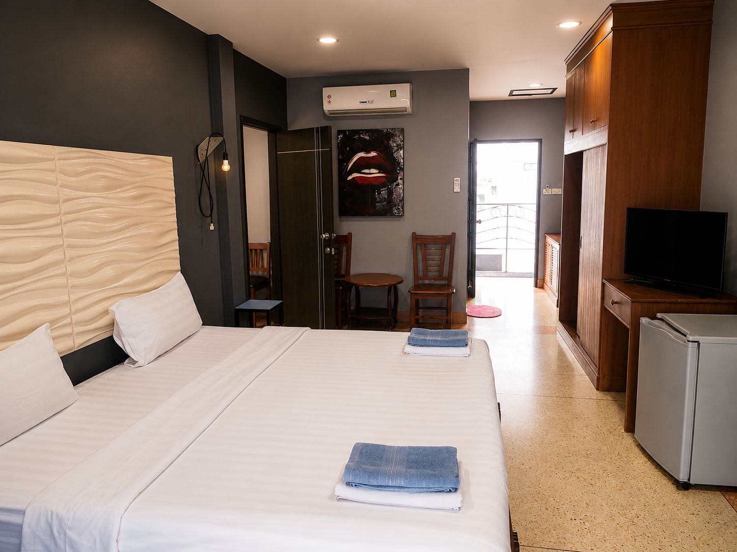 A hotel room with a bed, a desk, a chair, a television, and an air conditioning unit.