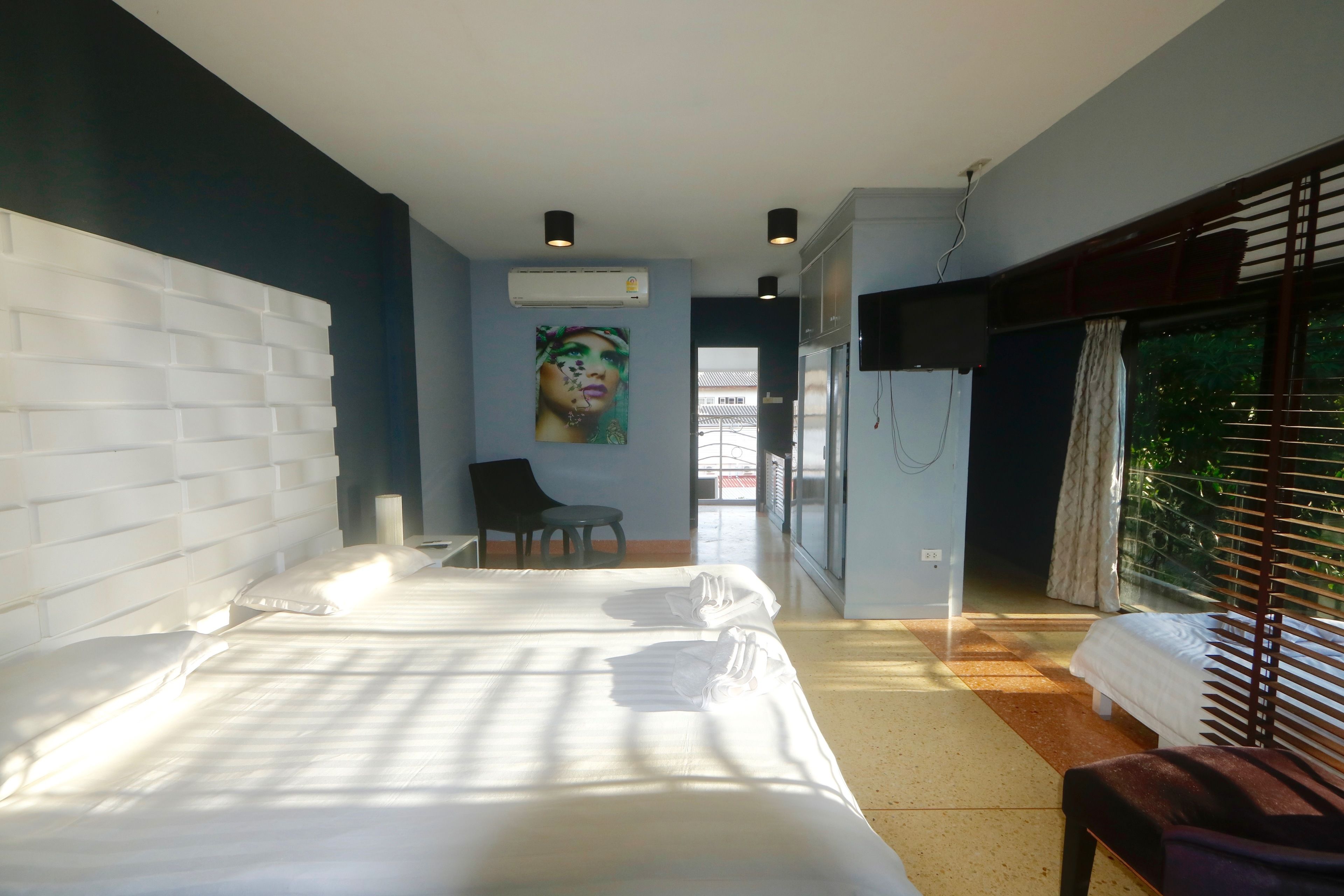A hotel room with a large bed, a chair, a desk, and a window with blinds.