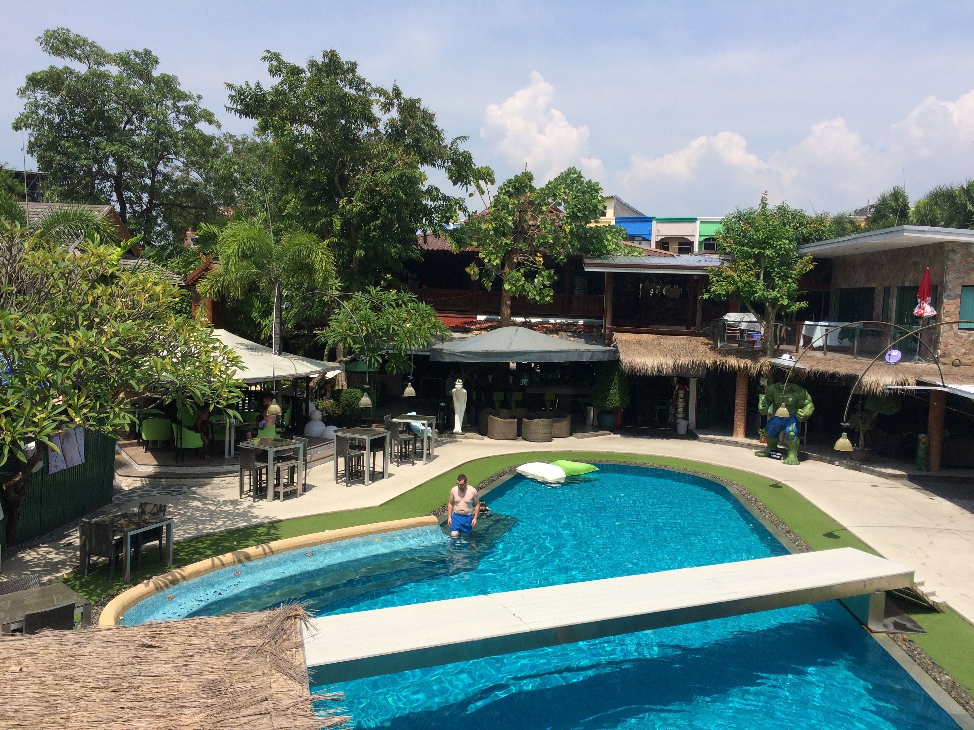 A swimming pool with a thatched roof structure, surrounded by outdoor seating and greenery.
