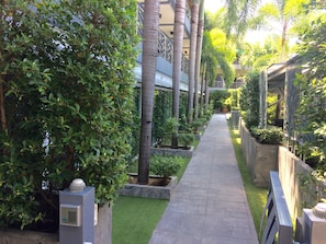 A pathway flanked by lush greenery and palm trees, leading to a building with a modern design. - Momento Resort (Pattaya)