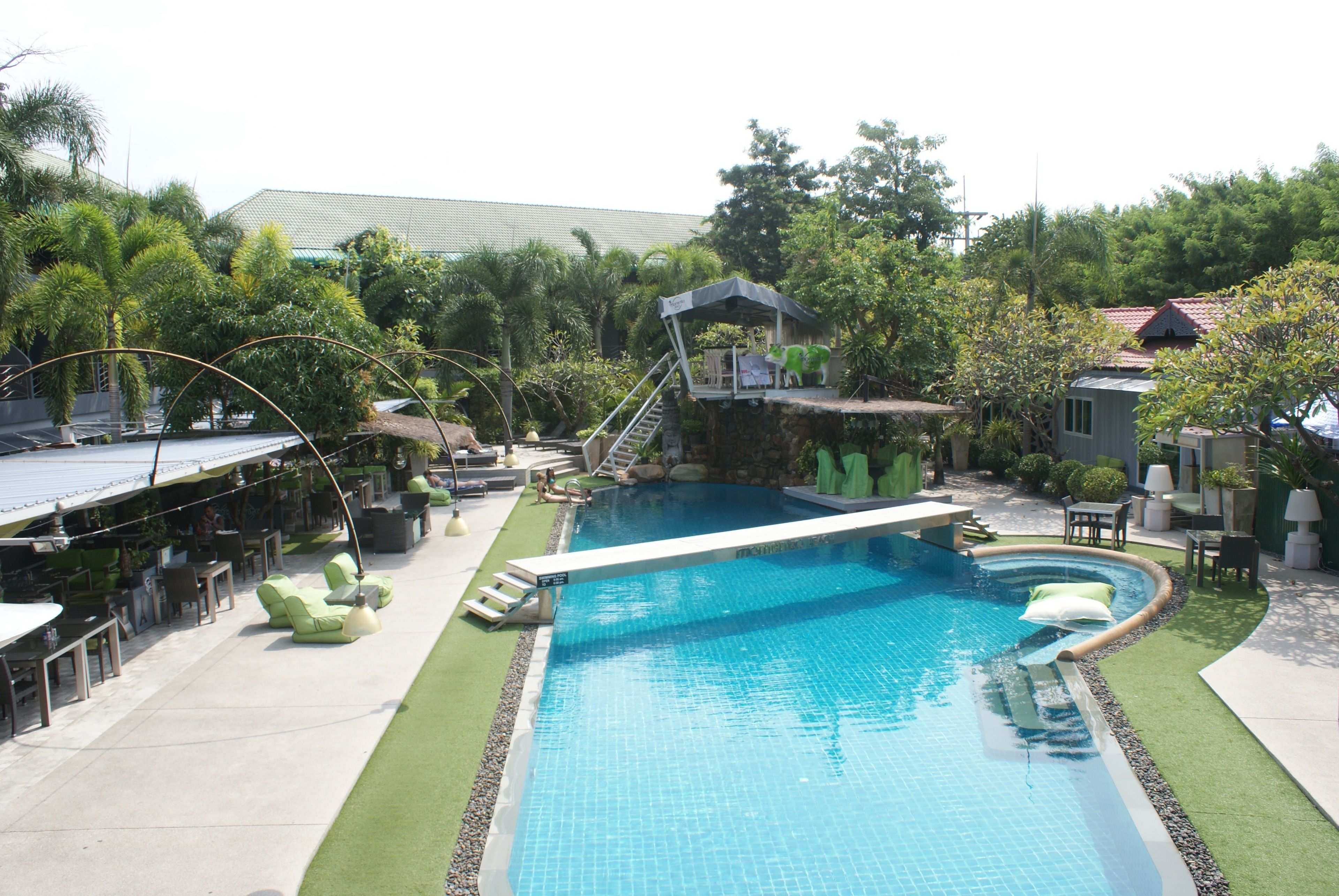 A swimming pool with a diving platform, lounge chairs, and a covered seating area.