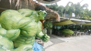 A large green statue of a muscular figure with a blue bag. - Momento Resort (Pattaya)